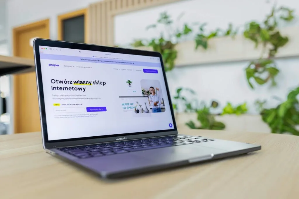 Laptop umieszczony na biurku, na ekranie widoczna makieta strony www, dotycząca otworzenia sklepu internetowego.
